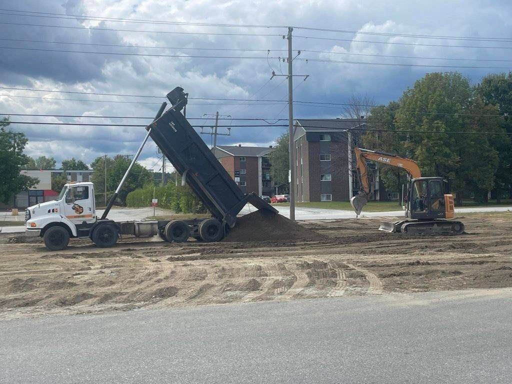 Camion-benne décharge terre sur chantier commercial avec excavatrice