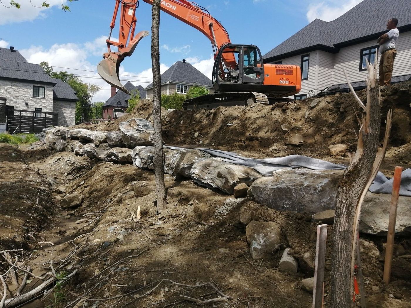 Grande excavatrice Hitachi place roches muret talus résidentiel