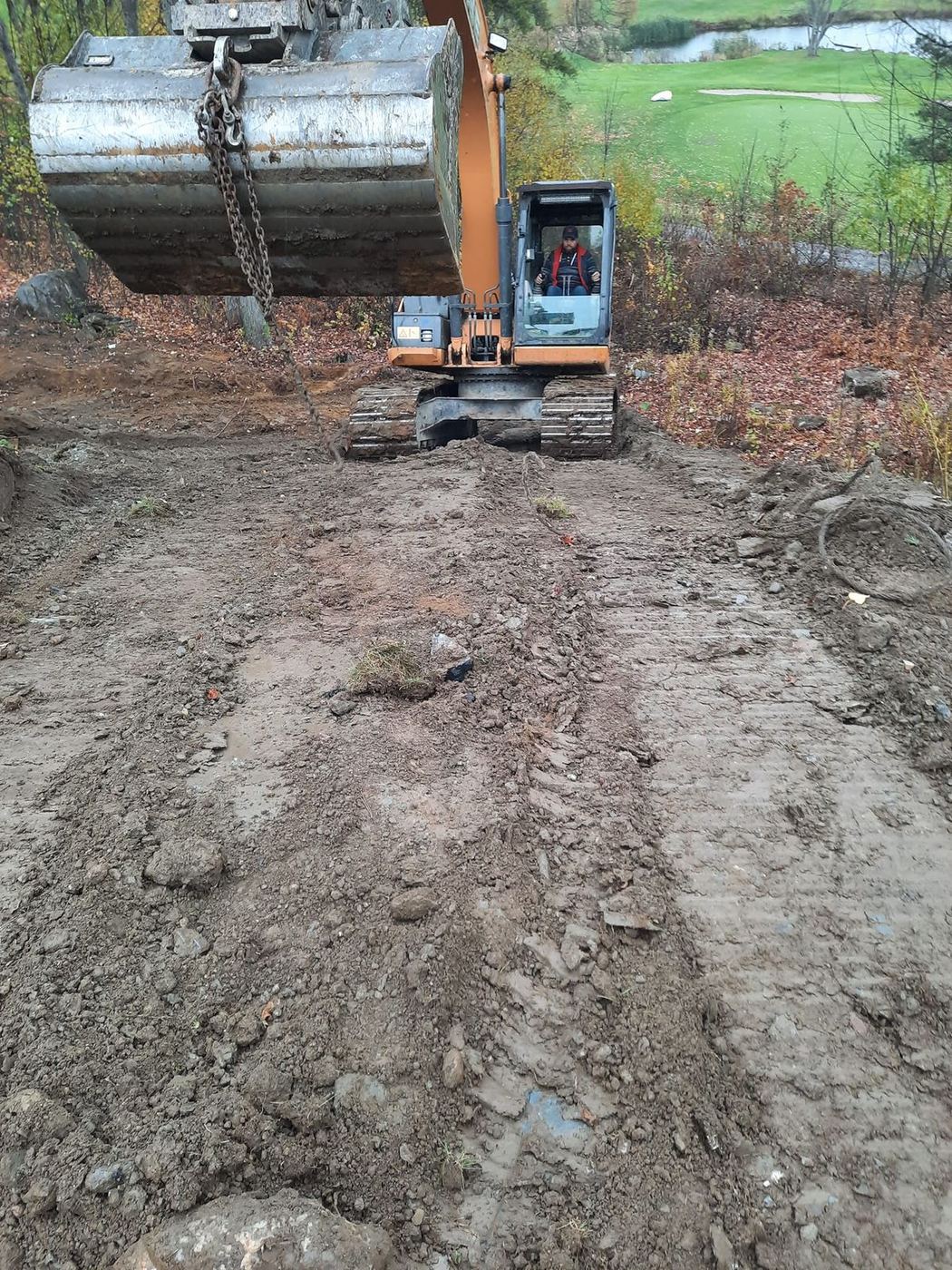 Grande excavatrice orange déblaye terrain boisé golf automne