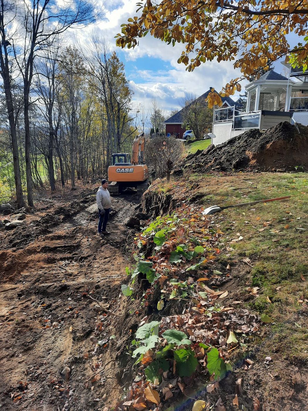 Grande excavatrice CASE et ouvrier, tranchée en talus boisé résidentiel