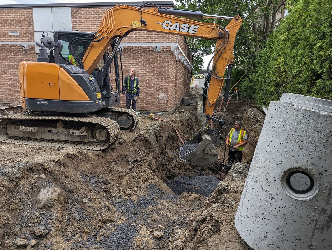 Excavatrice CASE creuse tranchée profonde près bâtiment commercial