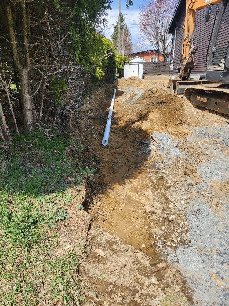 Tranchée ouverte avec tuyau PVC, excavatrice compacte en arrière-plan