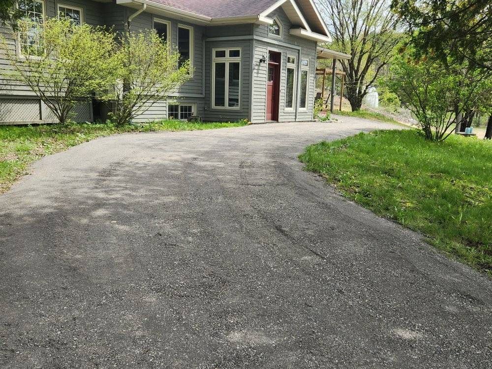 Entrée résidentielle asphaltée devant maison grise avec garage