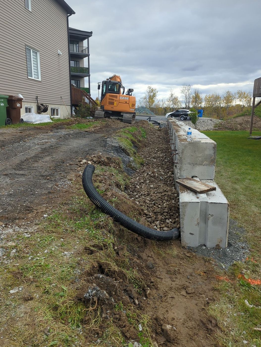 Muret blocs béton avec drain français et excavatrice en fond