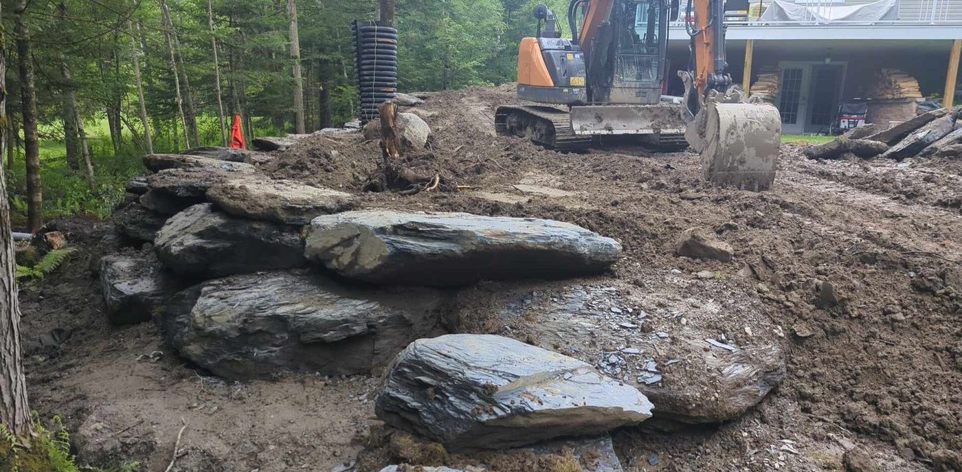 Excavatrice et roches lors déboisement terrain boisé résidentiel