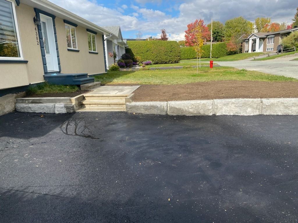 Entrée asphaltée neuve avec muret béton et escalier paysager